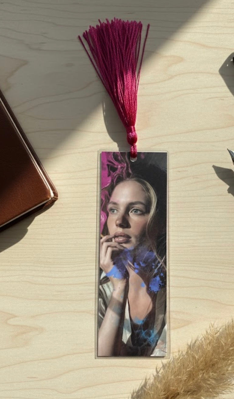 Bookmark with a portrait of a woman and floral design on a wooden surface with a red tassel.