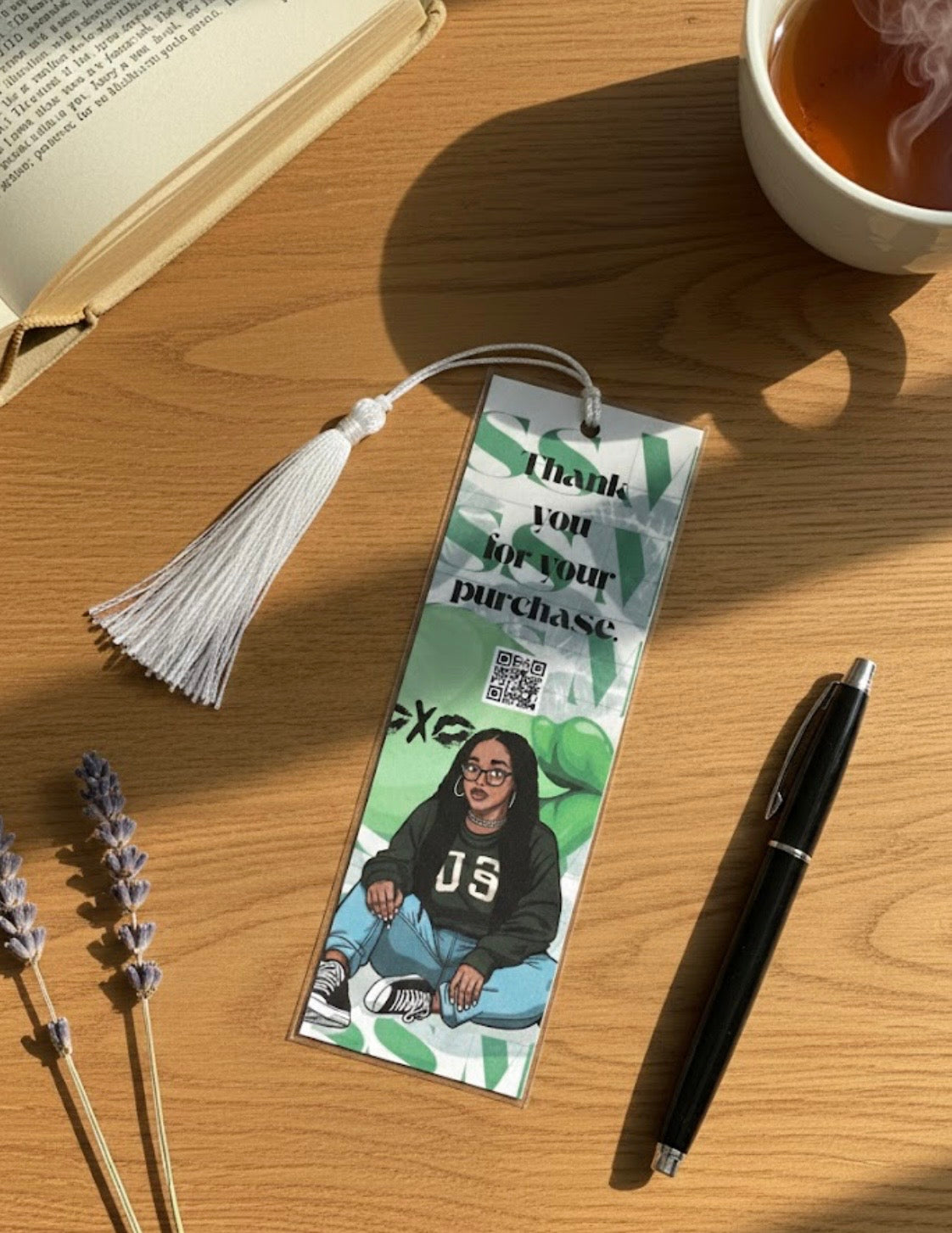 Bookmark with a photo of a person and text on a wooden surface with a book and cup of tea.