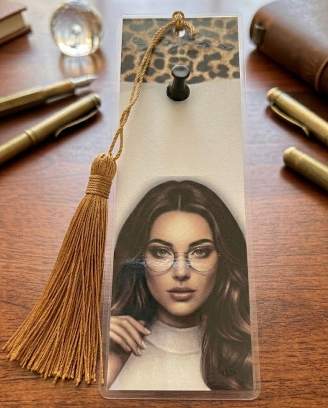 Bookmark with a portrait of a woman and a tassel on a wooden surface with pens.