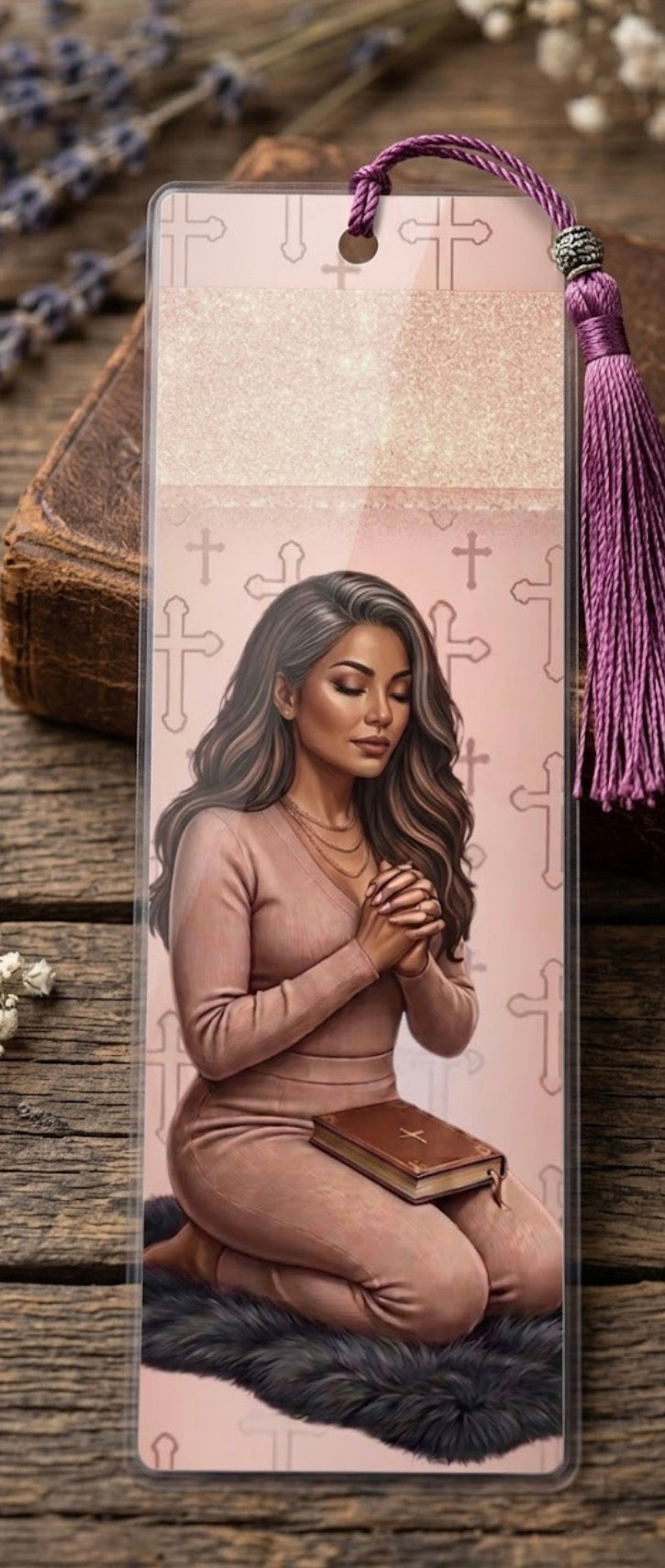 Bookmark with a design of a woman praying, placed on a wooden surface with lavender flowers.
