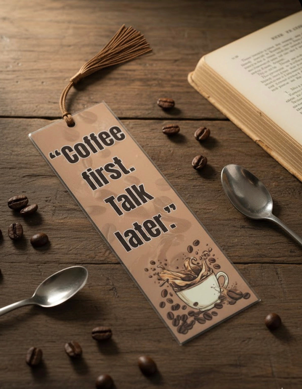 Bookmark with 'Coffee first. Talk later.' text on a wooden surface with coffee beans and spoons.