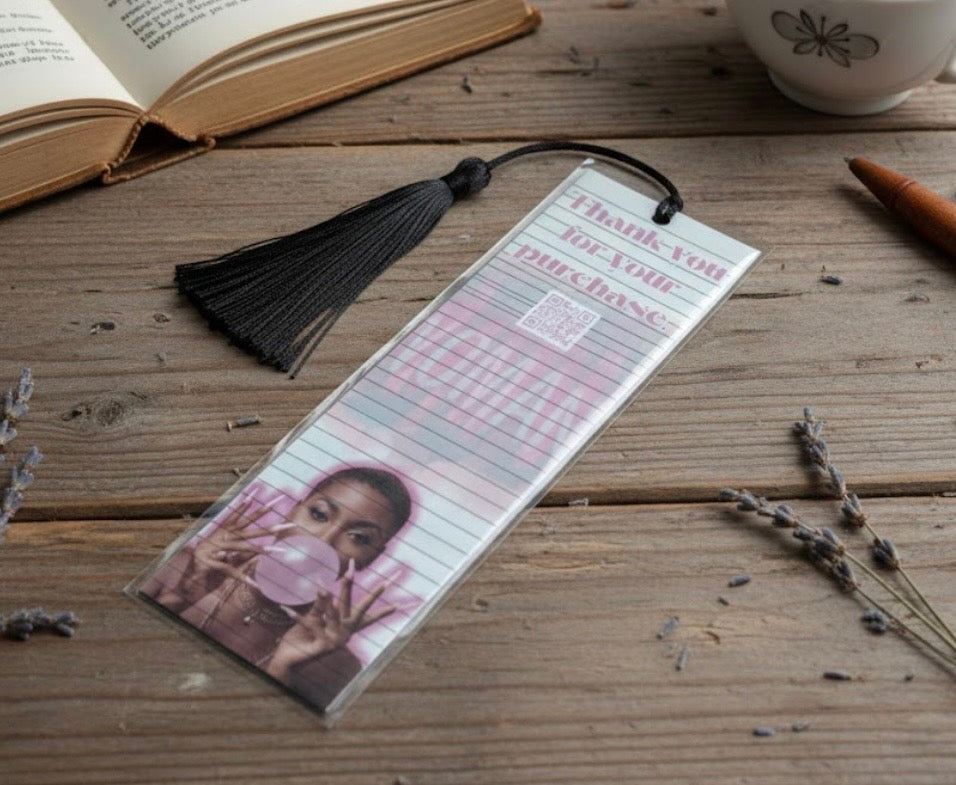 Bookmark with a photo of a child blowing a bubble, placed on a wooden surface with a book and mug in the background.