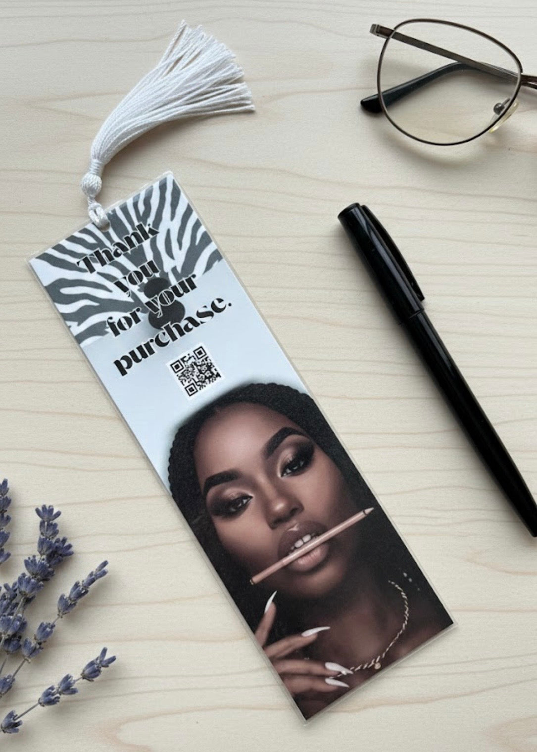 Bookmark with a portrait of a woman, pen, glasses, and lavender on a light surface