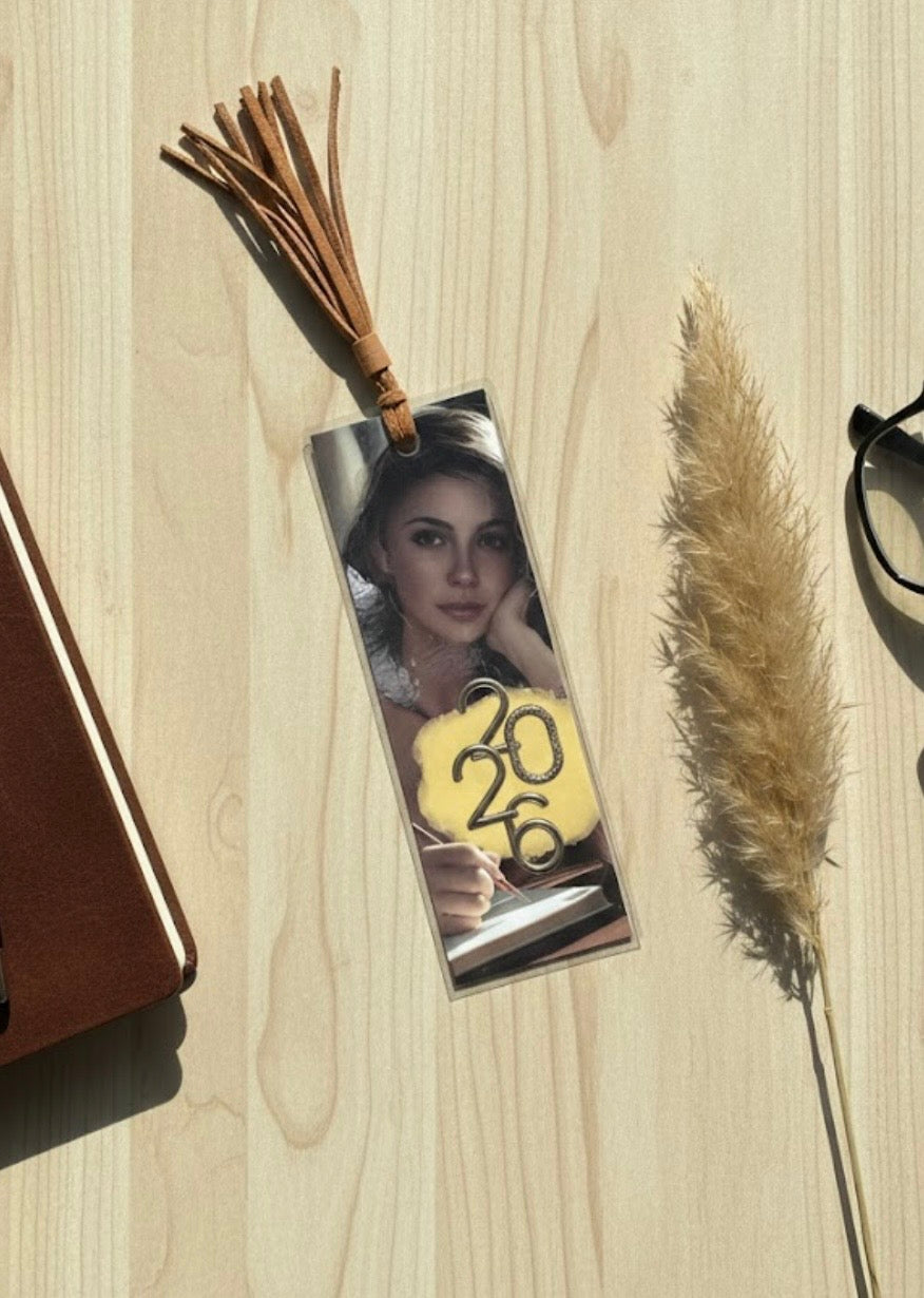 Bookmark with a photo of a woman and '2026' on a wooden surface with dried plants.