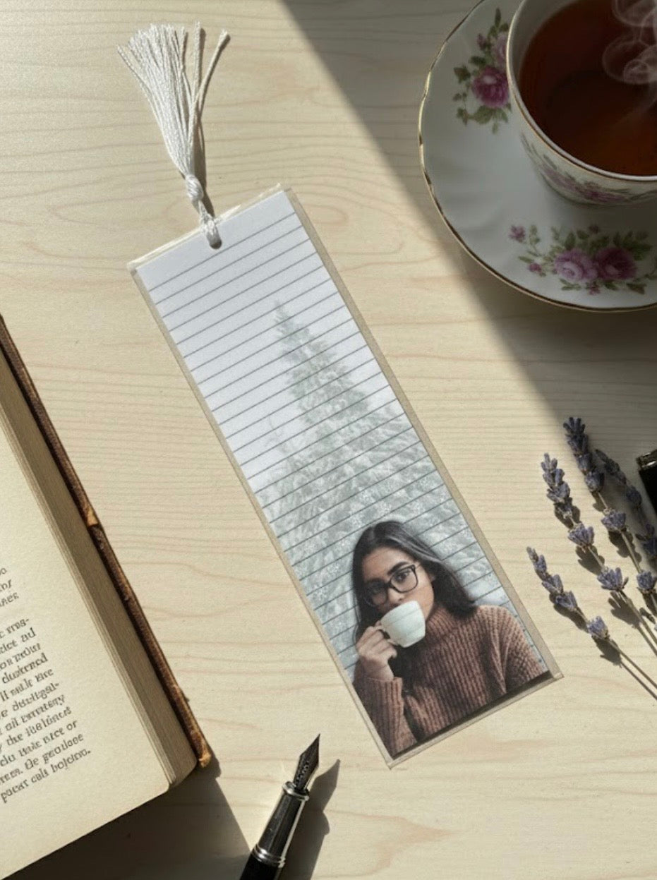 Bookmark with a photo of a person holding a cup, placed on an open book with a cup of tea and lavender flowers.