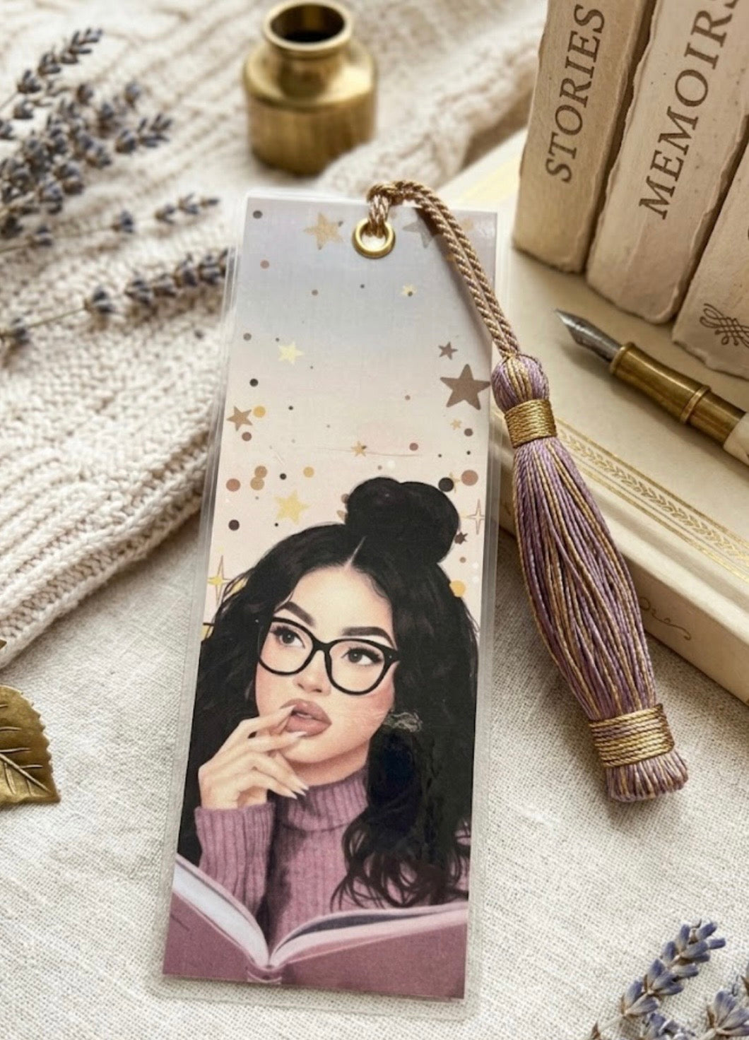 Bookmark with illustration of a person wearing glasses and reading a book, placed on a textured surface with books and lavender flowers.