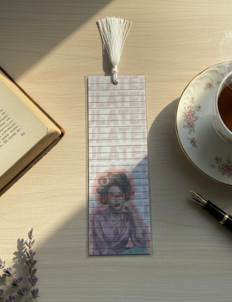 Bookmark with a character design on a table with a book, tea cup, and pen.