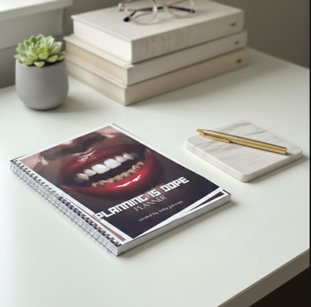 Planner with a graphic design on a desk with books and a plant.